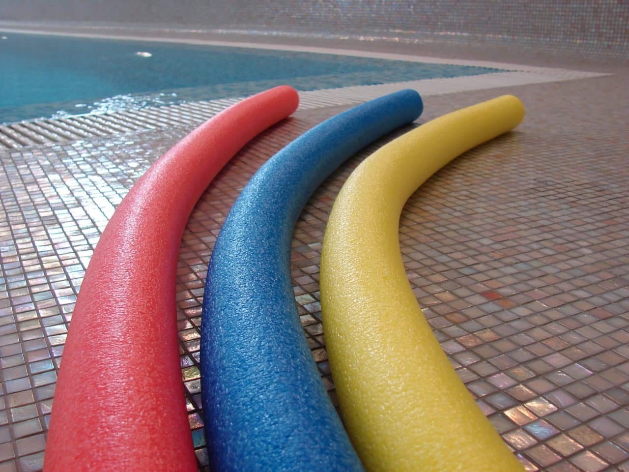 Three pool noodles laying on the ground next to an indoor swimming pool.
