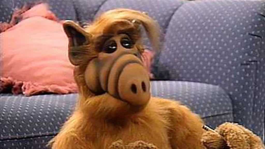 Alf (alien) sitting on the floor next to a couch 