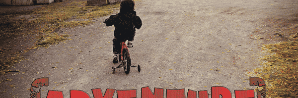 Young child riding a bicycle with training wheels on a dirt driveway