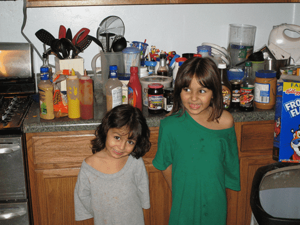 Two young children standing in front of a counter full of condiments preparing to make themselves a "different" snack.