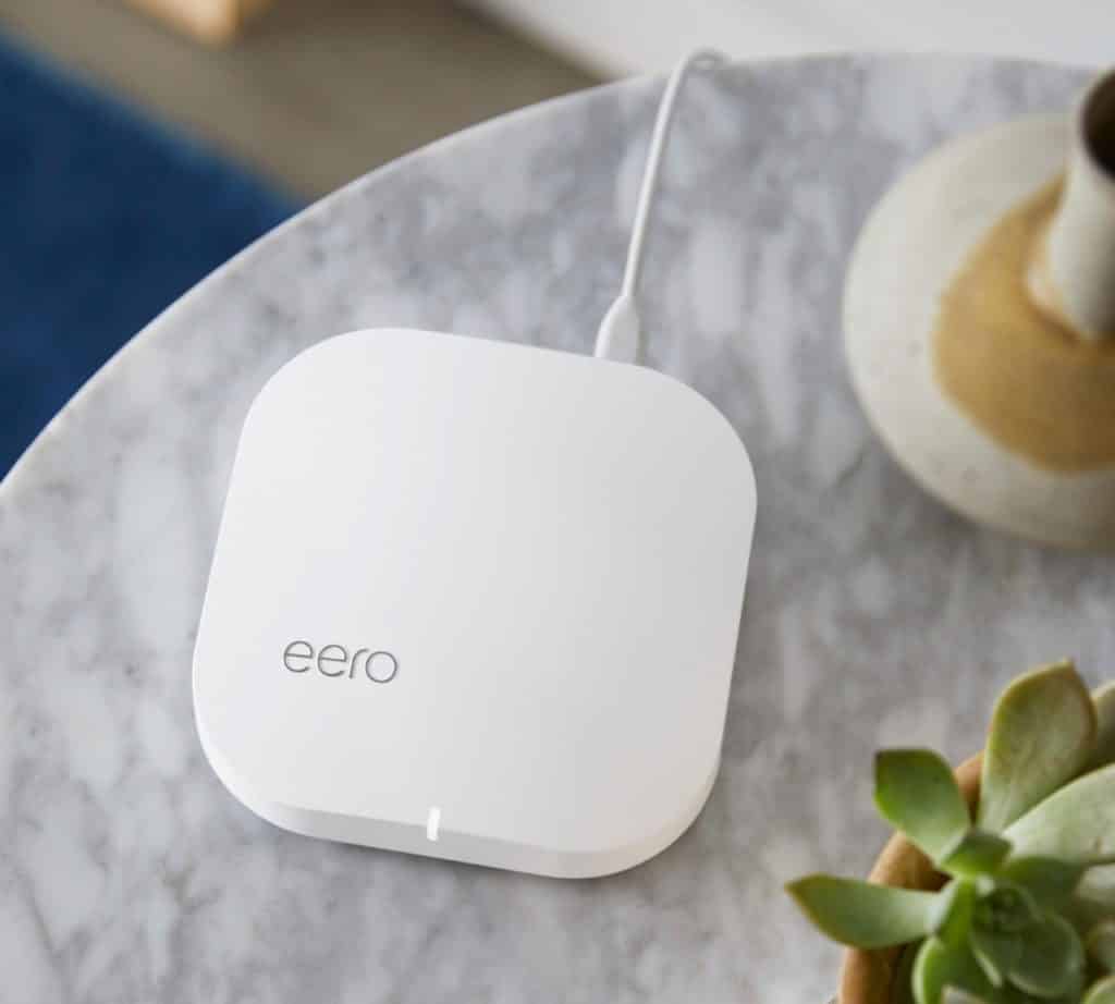 Closeup of an Eero wifi booster device sitting on a table next to a potted cactus