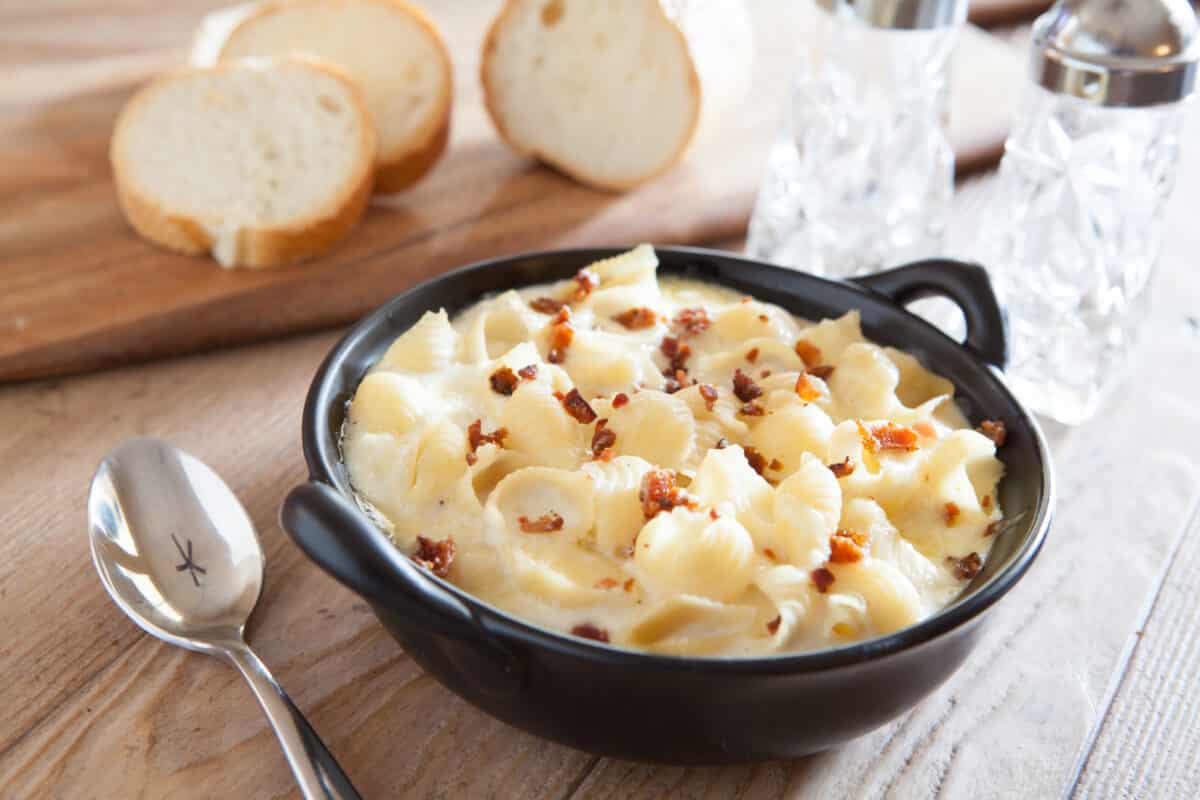 Creamy pasta and cheese in a bowl on a table. Next to the bowl is a few slices of french bread ready to be dipped in the creamy sauce.