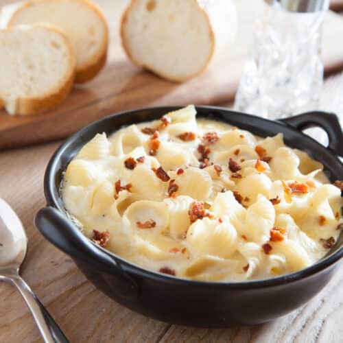 Creamy pasta and cheese in a bowl on a table. Next to the bowl is a few slices of french bread ready to be dipped in the creamy sauce.