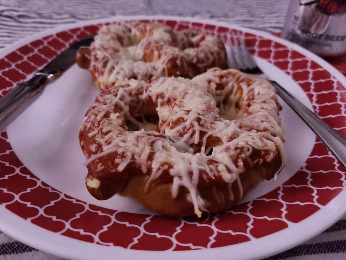A soft pretzel covered with marinara and mozzarella cheese on a plate with a fork and knife